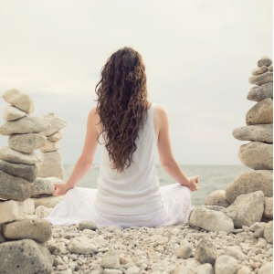 Frau meditiert am Meer zur Förderung der hormonellen Balance und inneren Ruhe