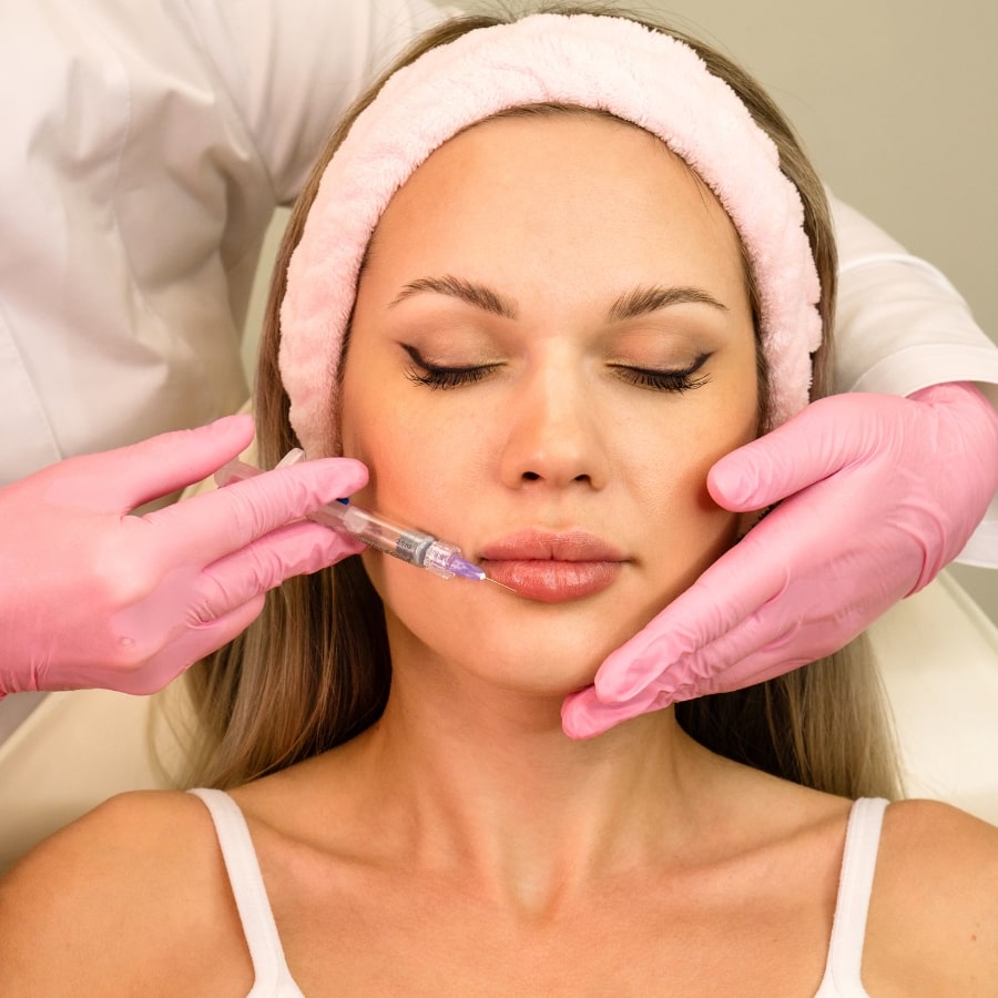 Frau bei einer Lippenunterspritzung mit Hyaluronsäure – ästhetische Behandlung durch Fachpersonal mit rosa Handschuhen.