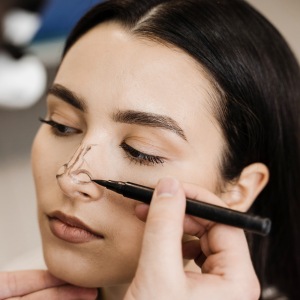 Frau bei der Vorbereitung auf eine ästhetische Nasenkorrektur – mit Markierungen auf der Nase durch medizinisches Fachpersonal.