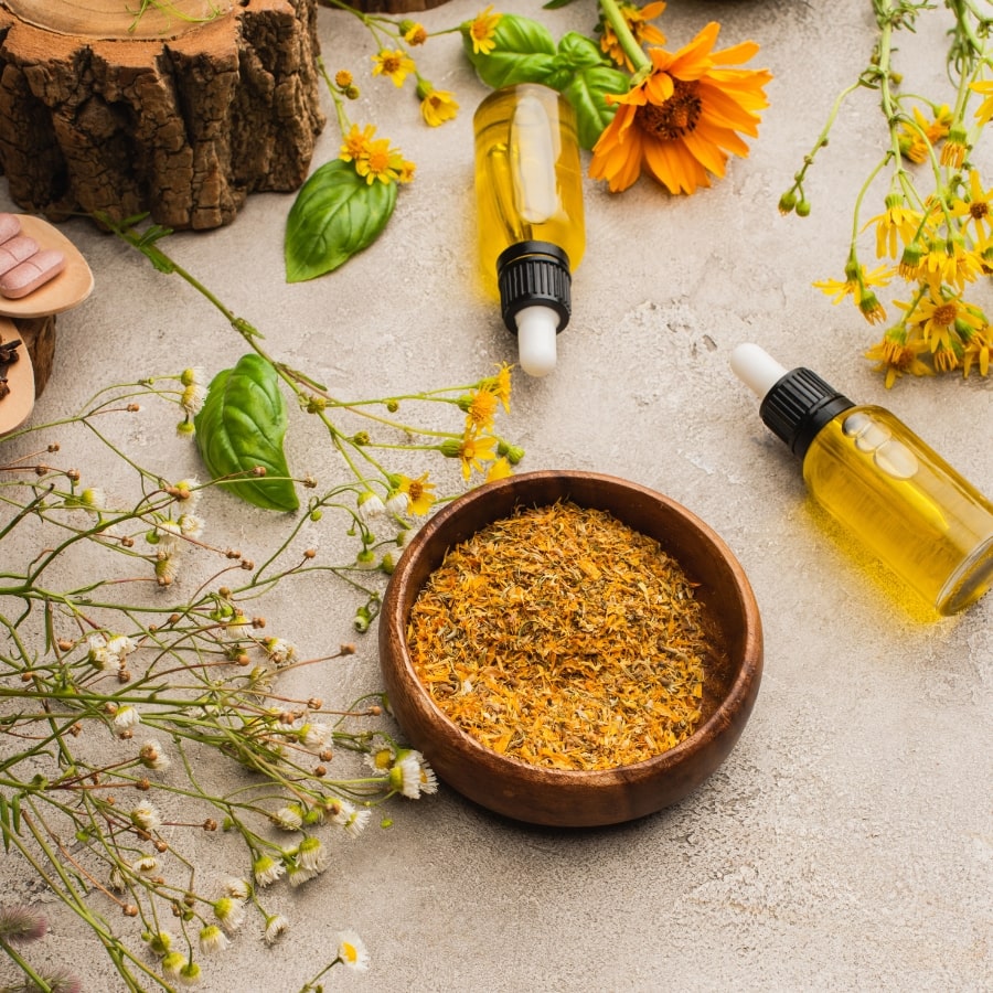 Getrocknete Heilkräuter in einer Holzschale, umgeben von Blüten und Fläschchen mit ätherischem Öl – Symbol für Naturheilkunde und pflanzliche Therapie.